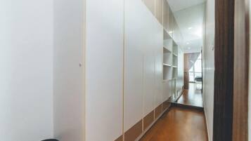 A narrow hallway with white walls and wooden flooring, leading to a room with a large window.