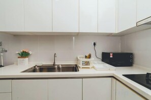 A kitchen with white cabinets, a stainless steel sink, a microwave, and a small potted plant. - Paragon Residence Johor Bahru (Johor Bahru)