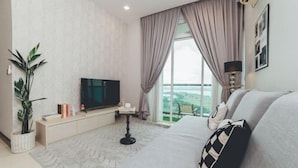 A modern hotel room with a large window, a flat-screen TV, a sofa, a bedside table, and a potted plant. - Paragon Residence Johor Bahru (Johor Bahru)