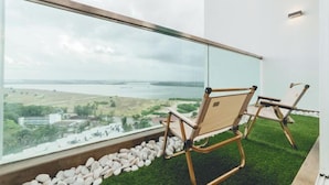 A balcony with a view of a lake and distant buildings, two wooden chairs, and a stone border. - Paragon Residence Johor Bahru (Johor Bahru)