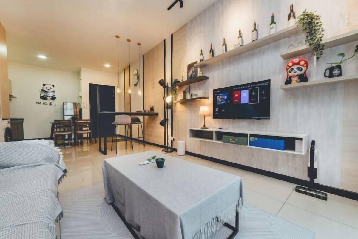 A modern living room with a sofa, a dining table, and a TV mounted on the wall.