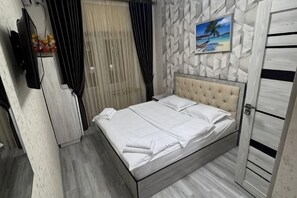 Un letto rifatto con lenzuola bianche, una TV a parete e un quadro a tema spiaggia.