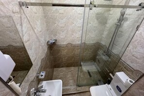 A glass-enclosed shower stall with a handheld showerhead, a handheld soap dispenser, and a white sink with a faucet. - Shosh Garden Family Resort (Bostanlik District)