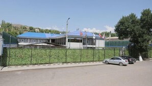 A building with a blue roof, a gated parking area, and a clear sky. - Shosh Garden Family Resort (Bostanlik District)