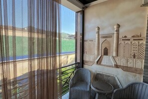 Varanda com cortinas leves, um mural de uma mesquita e duas cadeiras de vime.