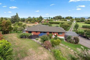 A house with a sloped roof, surrounded by a well-maintained lawn and trees. - Rotorua Family Retreat Hamurana 10000Sqm Lawn (Hamurana)