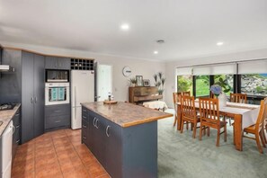 Cocina moderna con una isla central, comedor con sillas de madera y vistas amplias a través de grandes ventanales.