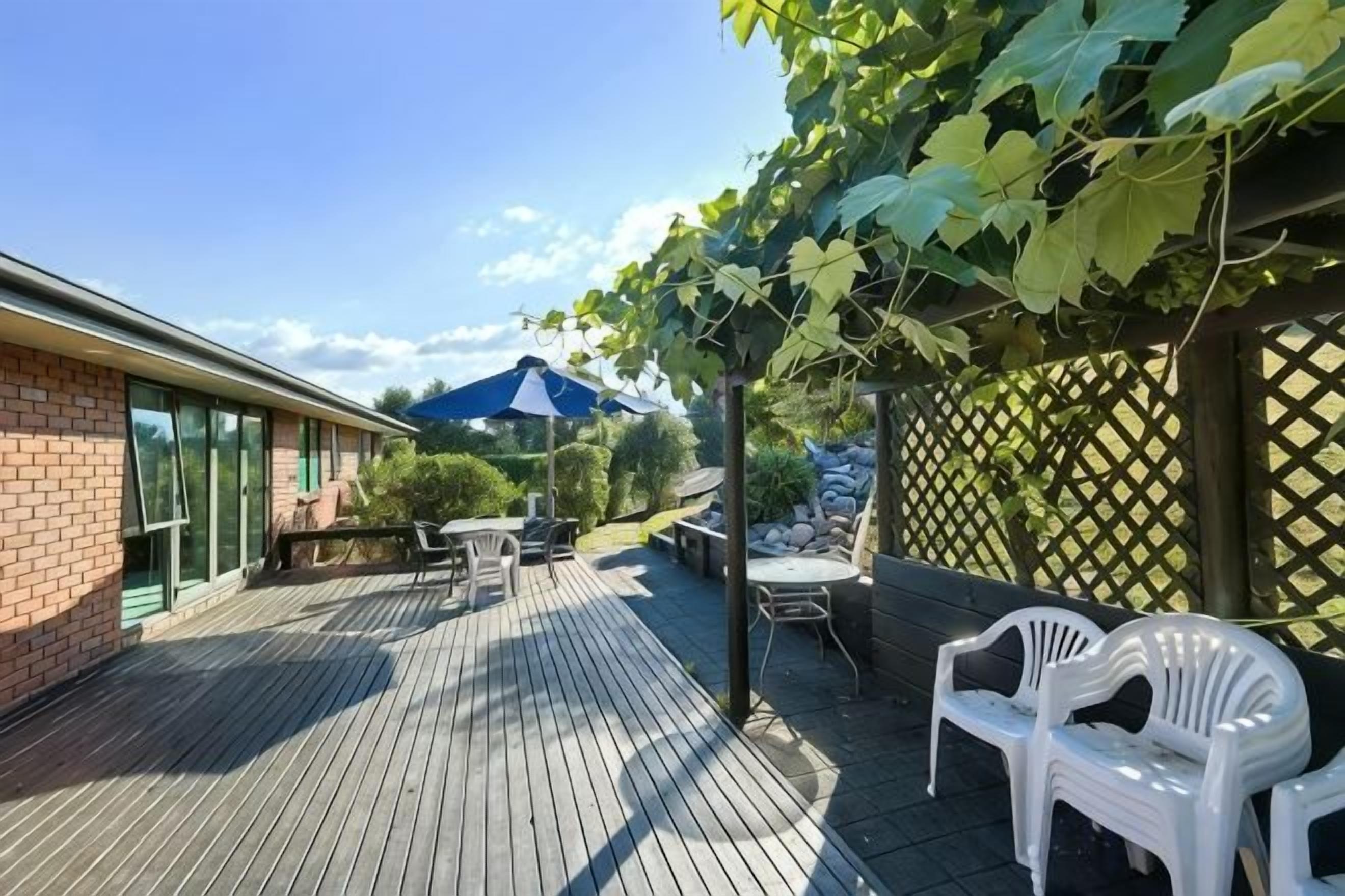 An outdoor patio with a wooden deck, a table and chairs, and a pergola with climbing plants.