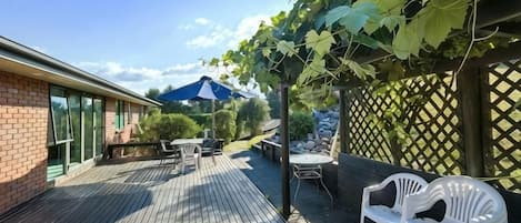 Une terrasse extérieure avec une plateforme en bois, une table et des chaises, et une pergola couverte de plantes grimpantes.