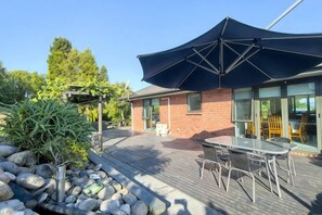 An outdoor patio with a table and chairs, a pergola, and a building with a glass door. - Rotorua Family Retreat Hamurana 10000Sqm Lawn (Hamurana)