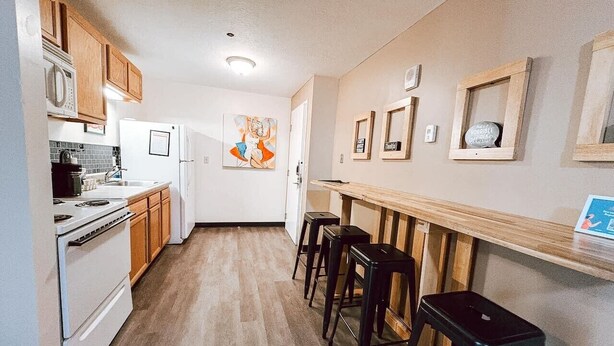 Une cuisine avec des meubles en bois, un réfrigérateur blanc, un four à micro-ondes, une cuisinière et un coin bar avec des tabourets.