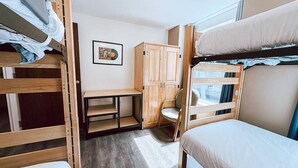 Une chambre avec un lit superposé, un bureau, une armoire en bois et une fenêtre.