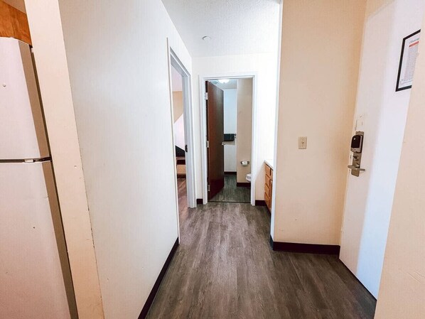 A narrow hallway with a wooden floor, leading to a bathroom and a kitchen area.