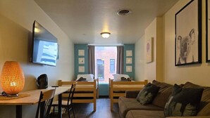 A room with a TV, bunk beds, a couch, a table, and a lamp. - Cozy + Convenient | Downtown Apt | Walk Everywhere (Pittsburgh)