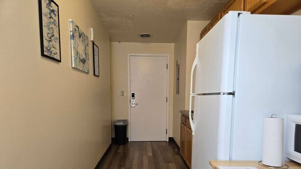 A narrow hallway with a wooden floor, a white door at the end, and a kitchen area with a refrigerator and microwave on the right. - Cozy + Convenient | Downtown Apt | Walk Everywhere (Pittsburgh)