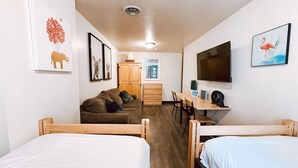 A room with two wooden beds, a wooden desk, a sofa, and a television on the wall. - Cozy + Convenient | Downtown Apt | Walk Everywhere (Pittsburgh)