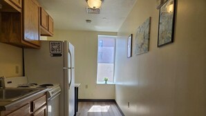 A narrow kitchen with wooden cabinets, a refrigerator, and a window with a view of the outside. - Cozy + Convenient | Downtown Apt | Walk Everywhere (Pittsburgh)
