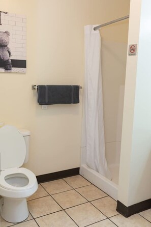 Un baño con inodoro, ducha con cortina blanca y toalla colgada en la pared.