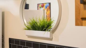 A kitchen with a round mirror, a plant in a white planter, black tiled backsplash, and wooden cabinets.
