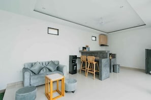 Un espace de vie moderne avec un canapé gris, une table basse en bois et un coin cuisine doté de tabourets de bar.