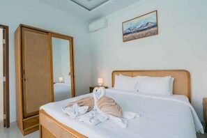 Une chambre d’hôtel avec un grand lit, une armoire en bois, un tableau au mur et un ventilateur de plafond.