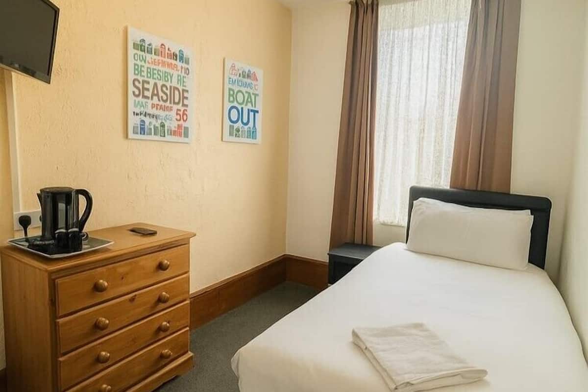 A hotel room with a bed, a wooden dresser, a coffee maker, and two wall decorations.