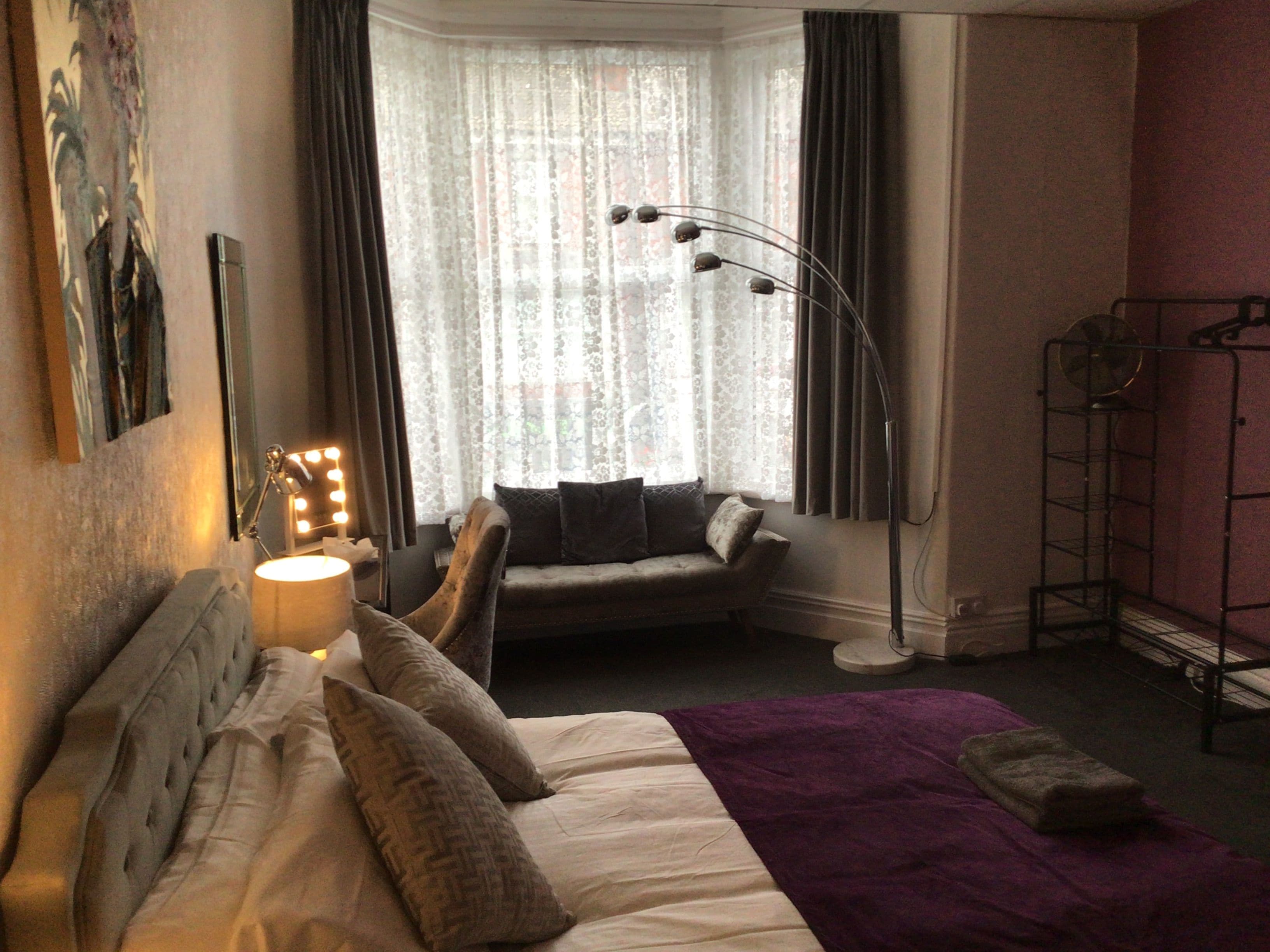 A hotel room with a bed, a seating area with a sofa, a standing lamp, and a window with curtains.