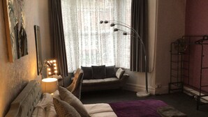 A hotel room with a bed, a seating area with a sofa, a standing lamp, and a window with curtains. - The White Swallow Hotel (Blackpool)