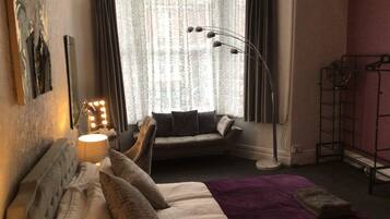 A hotel room with a bed, a seating area with a sofa, a standing lamp, and a window with curtains.