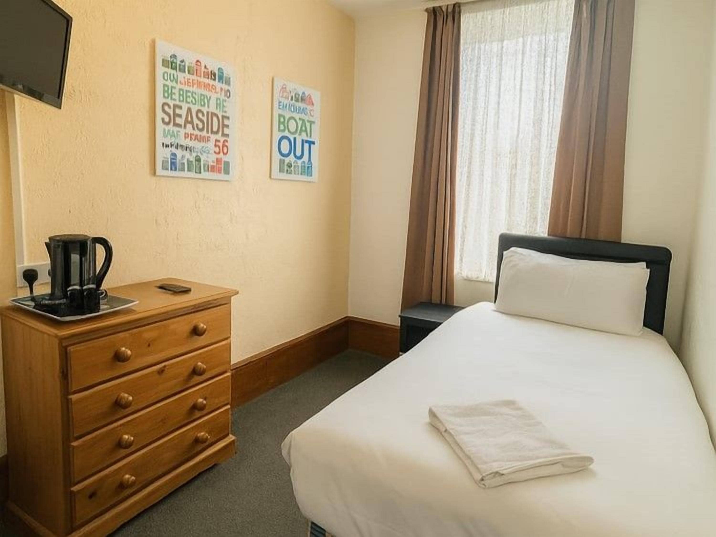 Ein Hotelzimmer mit einem Bett, einer Holzkommode, einer Kaffeemaschine und zwei Wandbildern.
