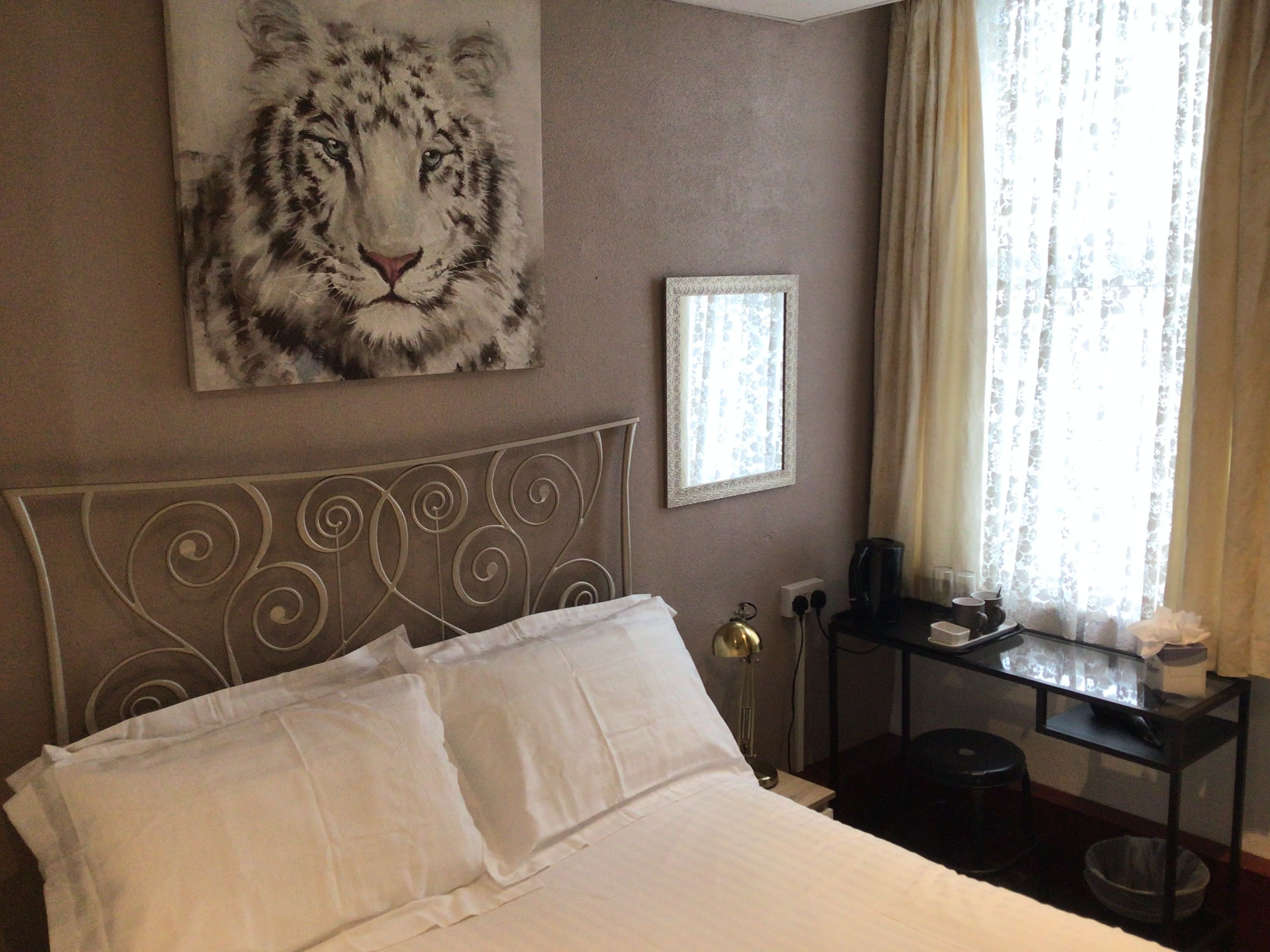 A hotel room with a bed, a painting of a tiger, a framed picture, a desk with a lamp, and a window with curtains.