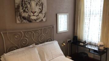 A hotel room with a bed, a painting of a tiger, a framed picture, a desk with a lamp, and a window with curtains.