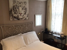 Een hotelkamer met een bed, een tijger schilderij, een lijst met een foto, een bureau met een lamp en een raam met gordijnen.