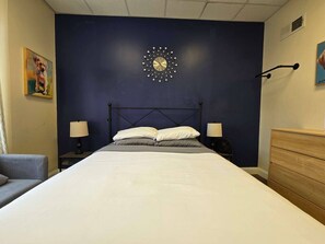 Un dormitorio con una cama grande, dos mesitas de noche con lámparas, un reloj de pared y un aparador.