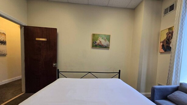 A hotel room with a bed, a sofa, a door, and a painting on the wall.