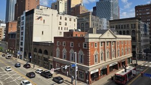 A cityscape with a variety of buildings, including a prominent red brick building with a classical facade and a modern glass skyscraper in the background.