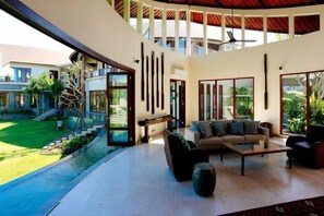 A modern interior with a curved ceiling, large windows, a seating area with sofas and a coffee table, and a view of a landscaped garden.