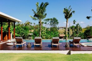 A poolside area with lounge chairs and a pool, surrounded by palm trees and greenery. - Umah Daun Villa by Nakula (Bali)