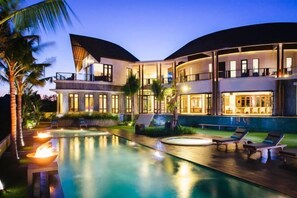 A modern resort with a large swimming pool, lounge areas, and a well-lit building with multiple levels. - Umah Daun Villa by Nakula (Bali)