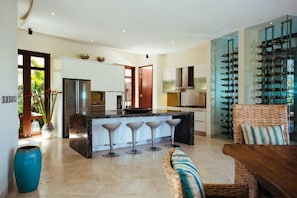 A modern kitchen with a central island, bar stools, and a wine rack. - Umah Daun Villa by Nakula (Bali)