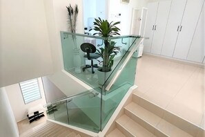 A modern interior with a glass railing staircase, a desk with a chair, and a potted plant.