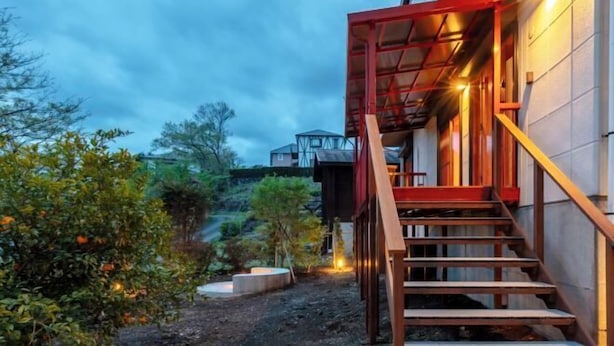 A staircase leading to a building with a red frame, surrounded by greenery and a clear sky. - VILLA + SECCA (Ito)