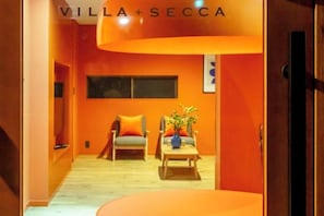 A modern interior with a curved orange wall, a wooden floor, and a seating area with two chairs and a table. - VILLA + SECCA (Ito)