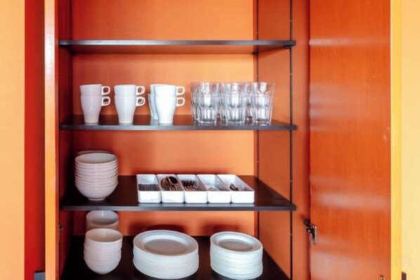 Un meuble de rangement avec des étagères contenant des tasses, des bols et des assiettes blancs.