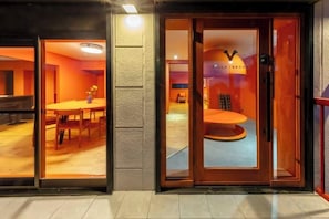 A hotel entrance with a glass door, a reception desk, and a seating area visible through the glass. - VILLA + SECCA (Ito)