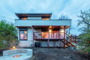 Une maison moderne à deux étages dotée d’un espace extérieur couvert, d’un foyer et d’un escalier menant à l’étage supérieur.