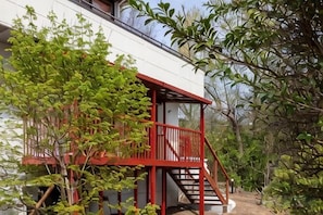 A building with a red staircase leading to a balcony, surrounded by greenery. - VILLA + SECCA (Ito)