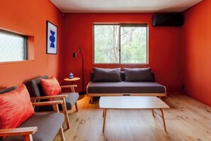 A compact room with a sofa, a small table, and a window with a view of trees. - VILLA + SECCA (Ito)