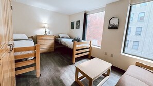 Une chambre de taille modeste, comprenant deux lits, un bureau, une chaise et une armoire.