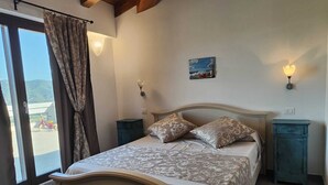 Un dormitorio con una cama, dos mesitas de noche, una mesita auxiliar, un ventanal con cortinas y vistas al exterior.
